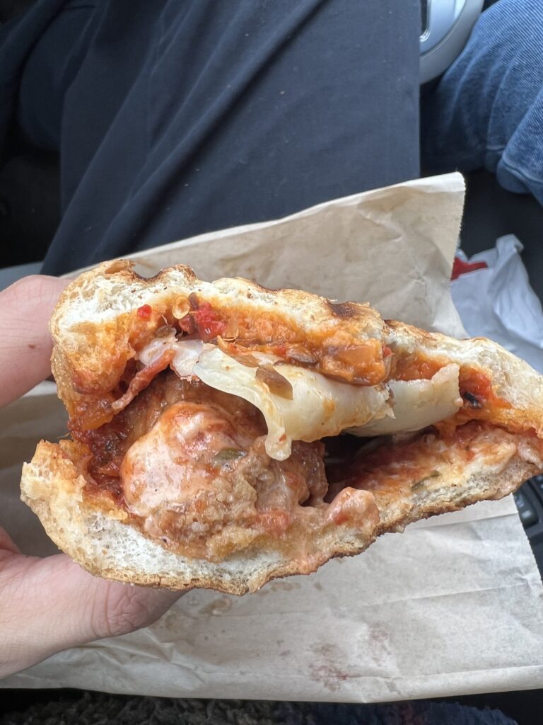 A close-up image of a man holding a meatball panini with one hand 
